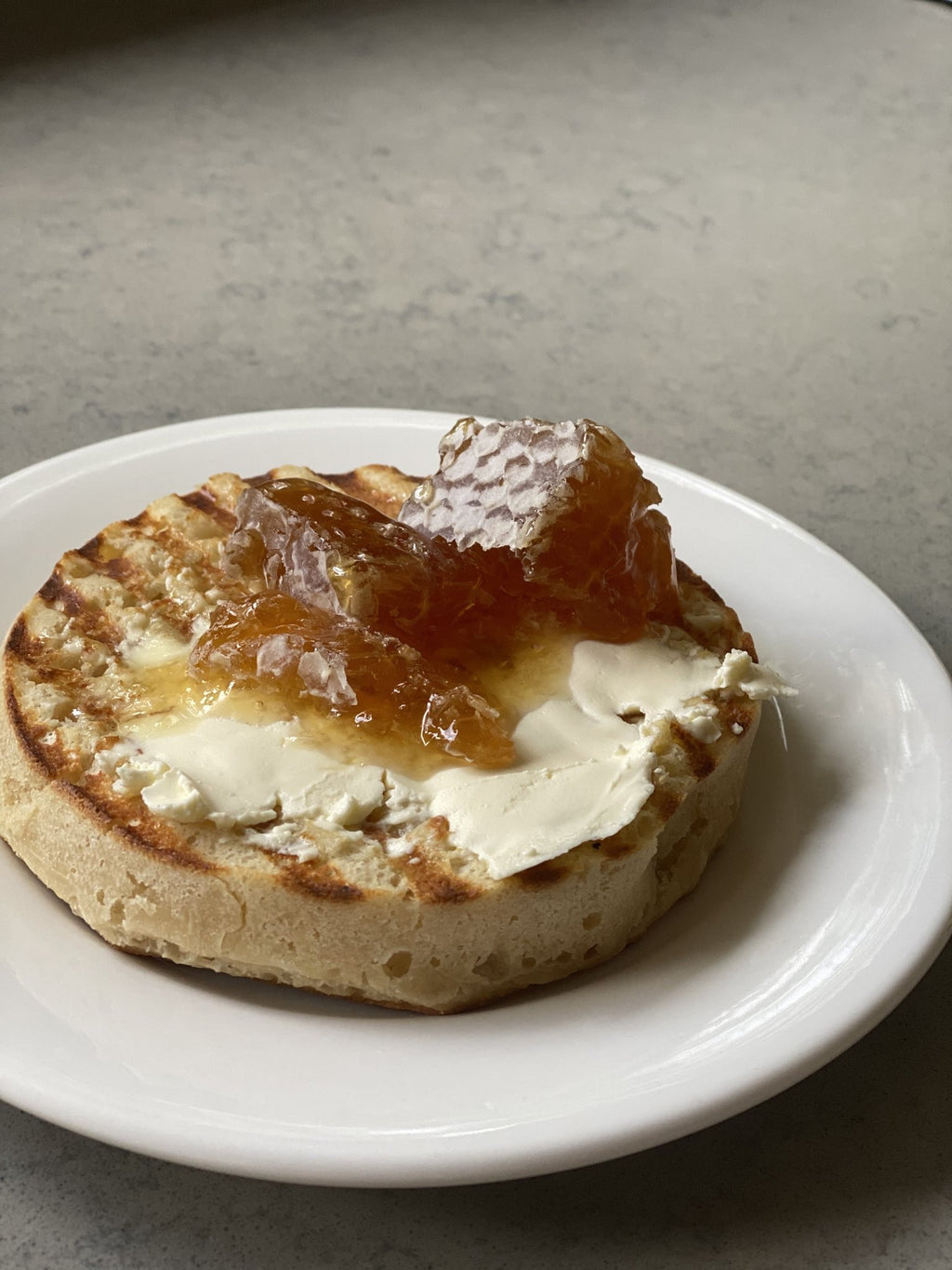 A piece of comb honey on a toasted crumpet with cream cheese